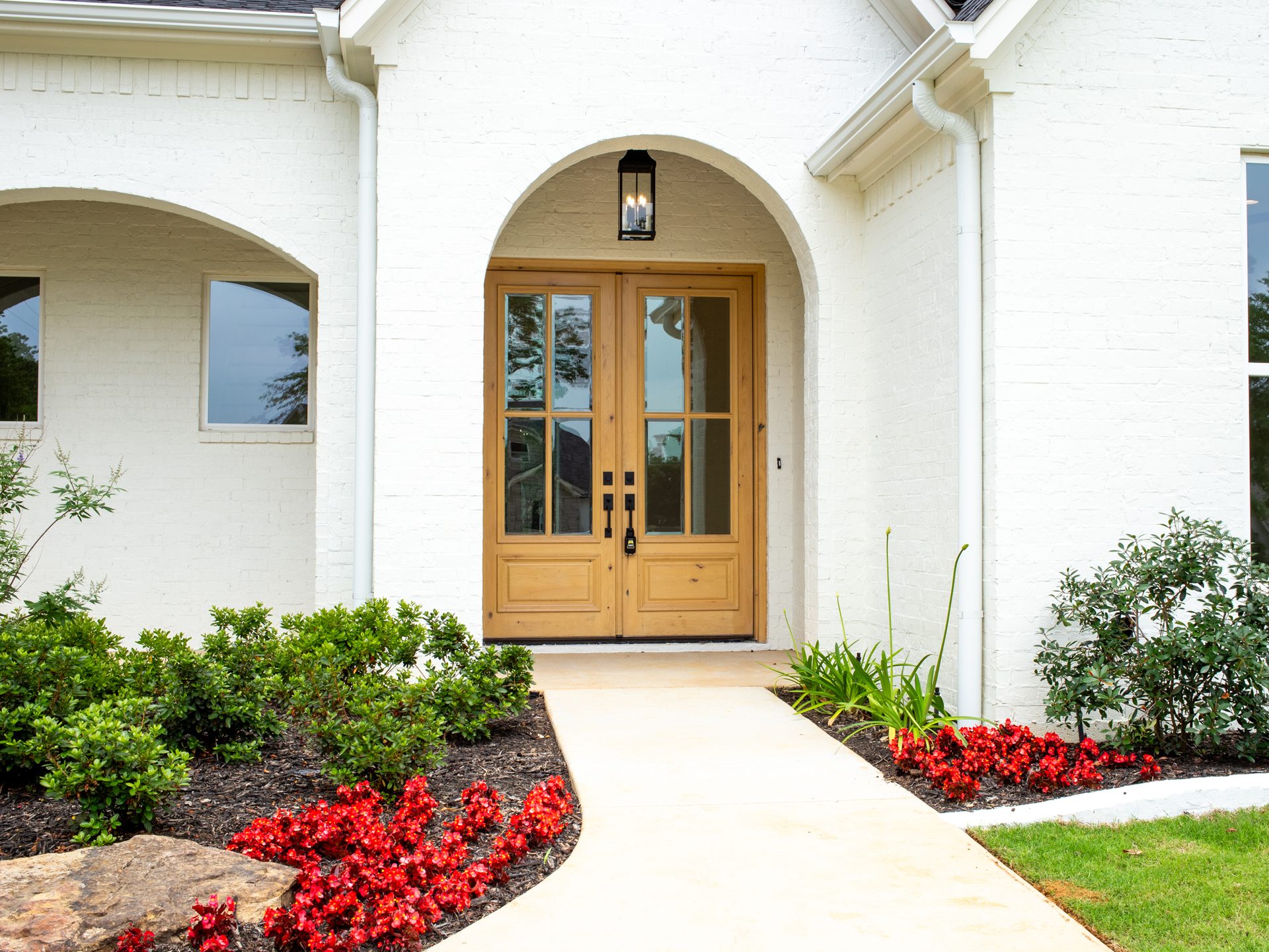 Arched wood entry doors on a white brick facade with red azaleas.