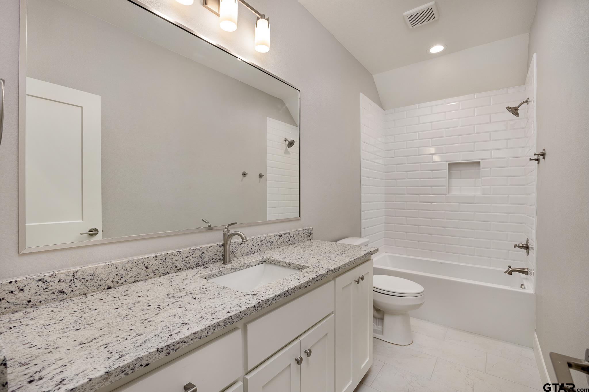 Guest bath with a granite vanity, framed mirror, white subway tile shower surround, and a soaking tub.