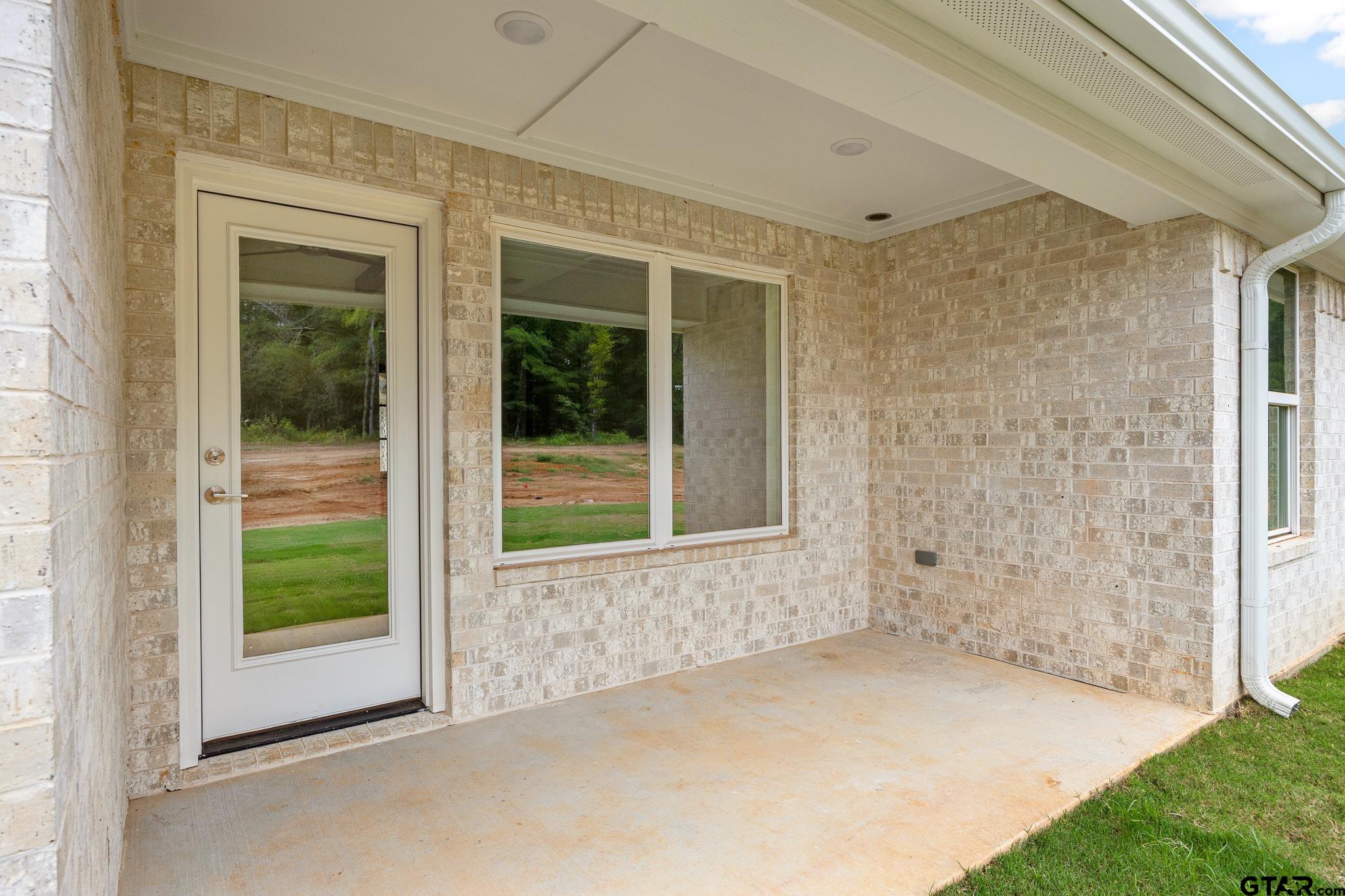Covered back porch with brick walls, a glass-paned back door, and a view to the wooded backyard.