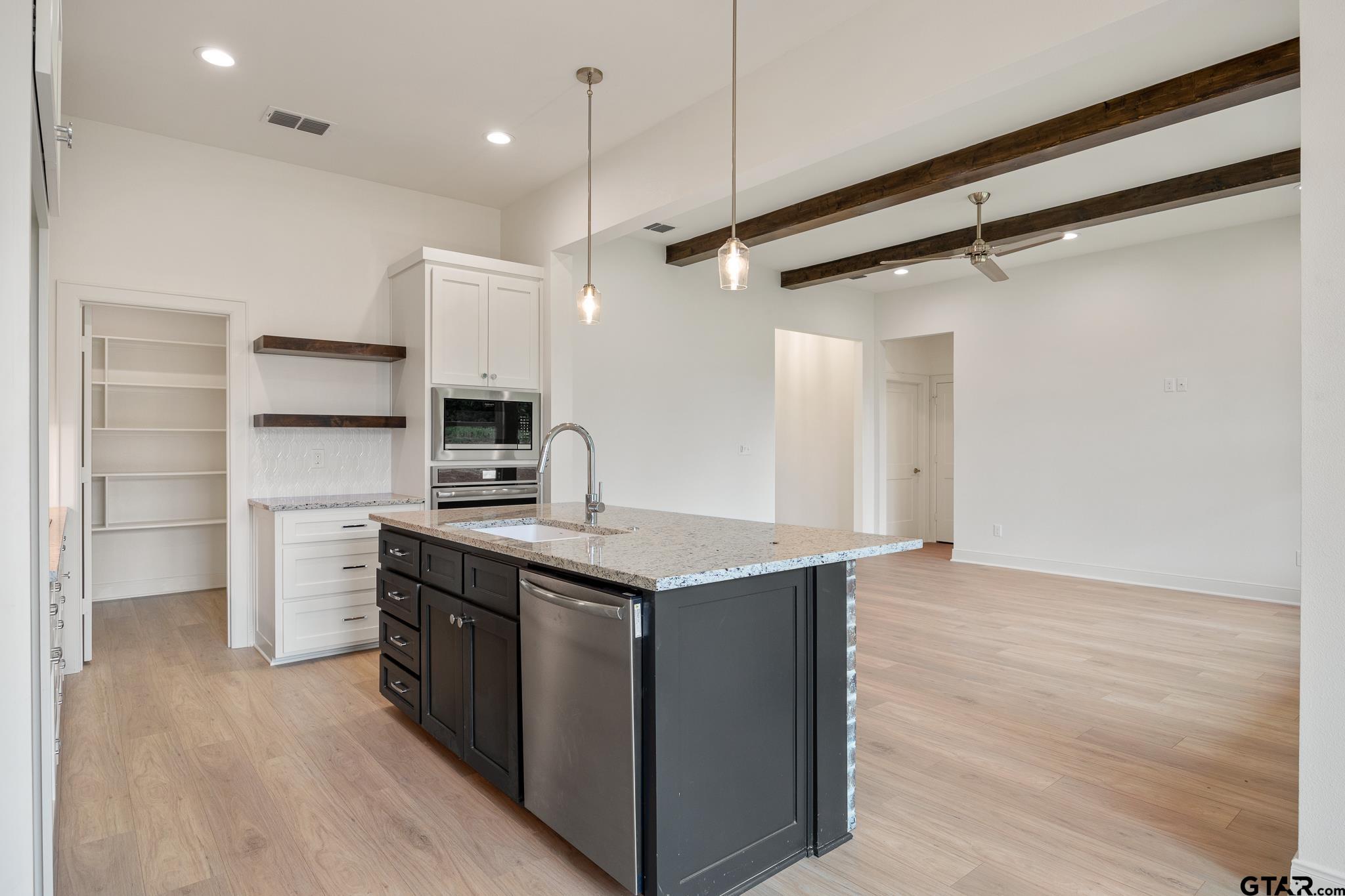 Open kitchen with white cabinets, granite island, and dark wood beams.