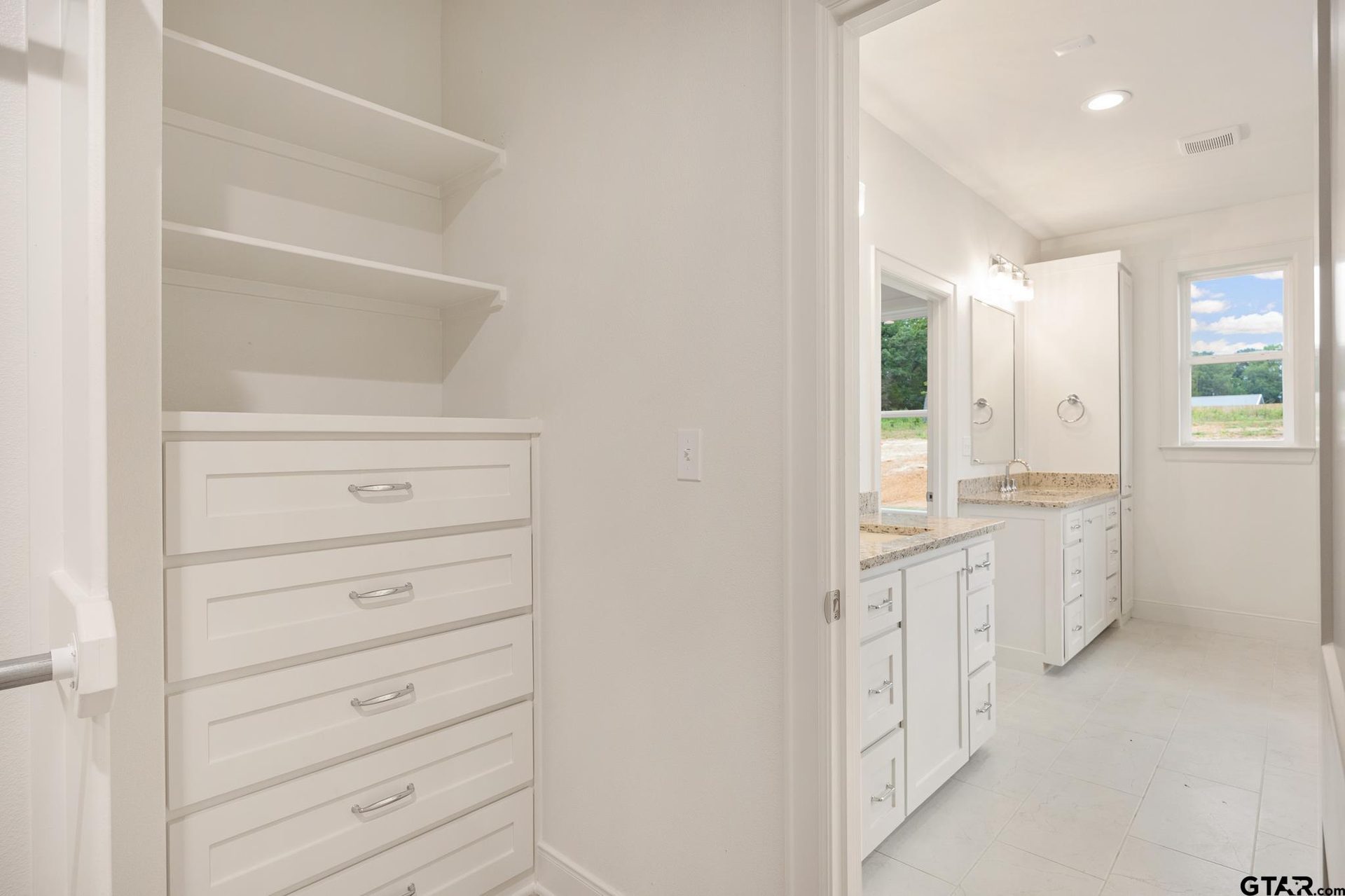 Primary walk-in closet with built-in drawers and open shelving, with a view through to the bathroom beyond.