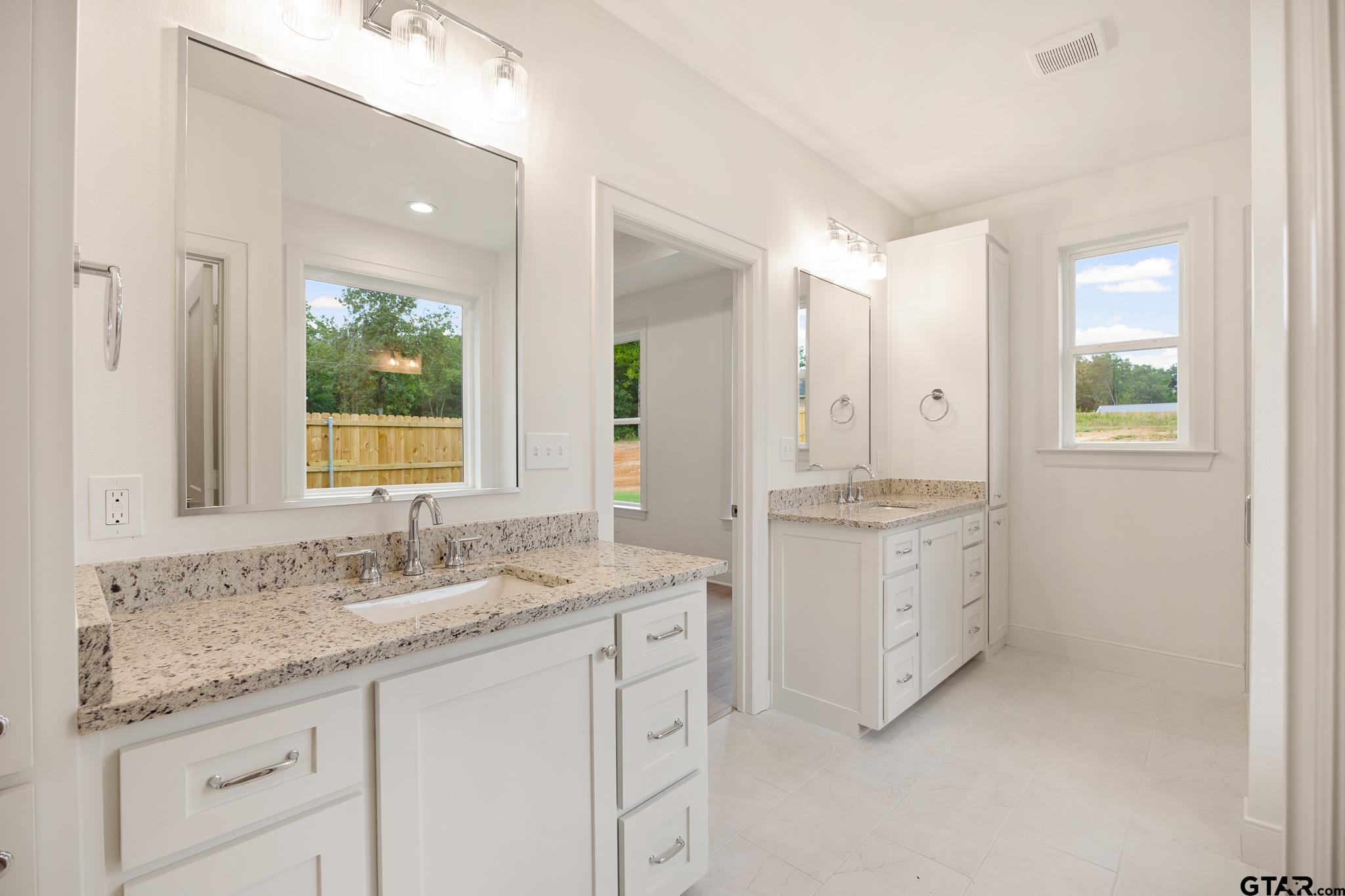 Primary bathroom with split vanities, white shaker cabinetry, granite counters, and a window view to the back pasture.