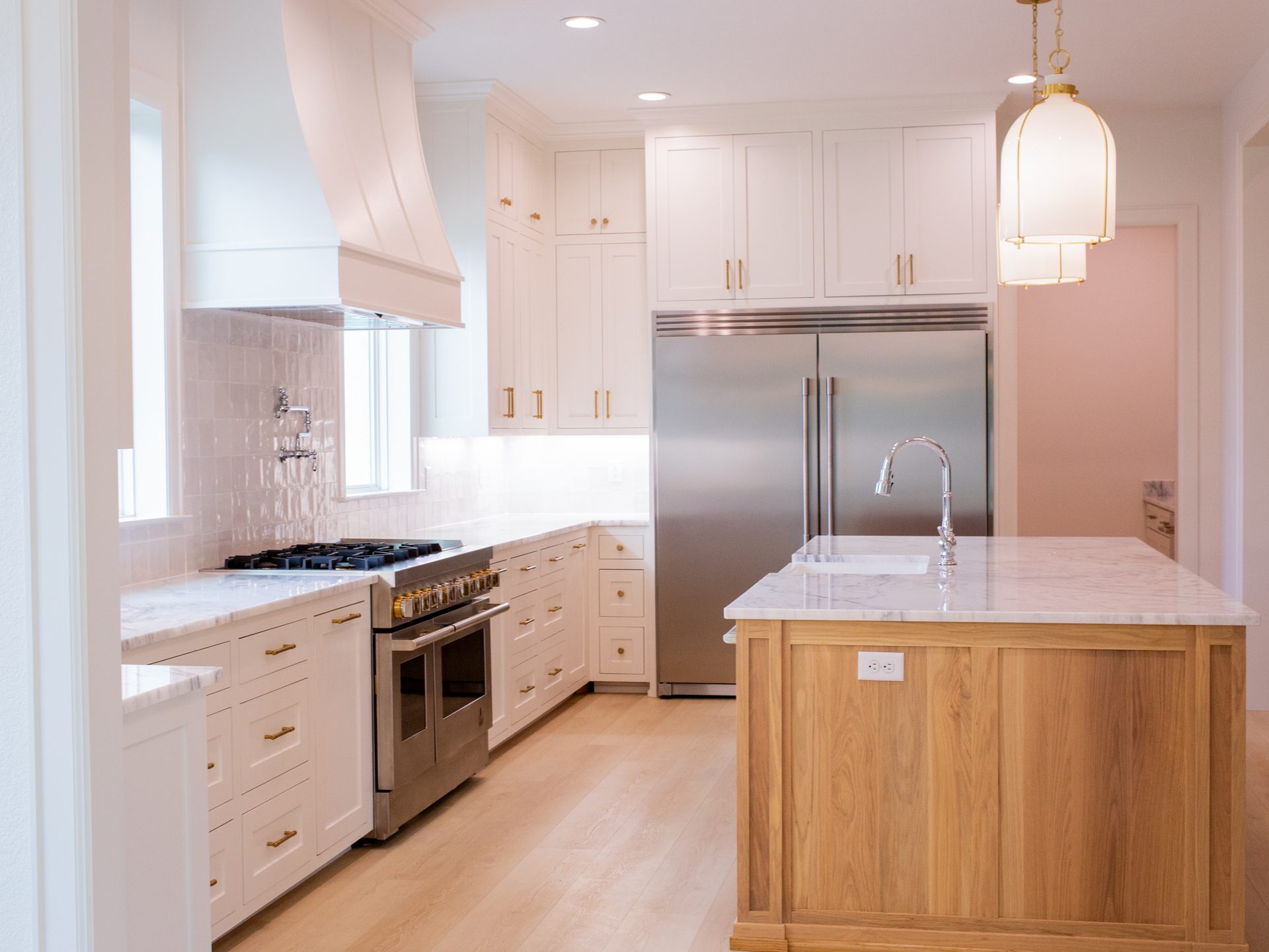 Custom kitchen with range hood, white cabinetry, and marble backsplash by Nicholas Humphrey Homes.