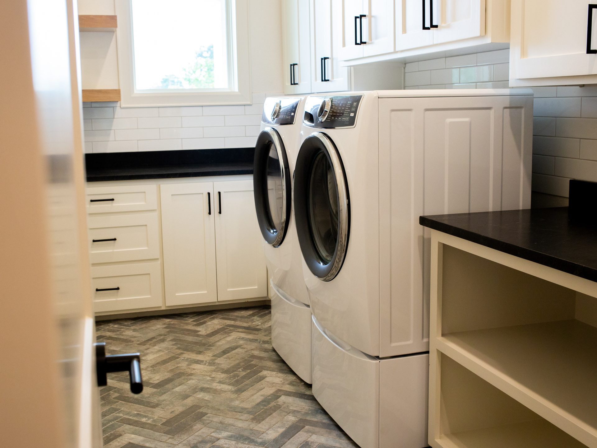 Laundry room with herringbone brick floor and white cabinetry.
