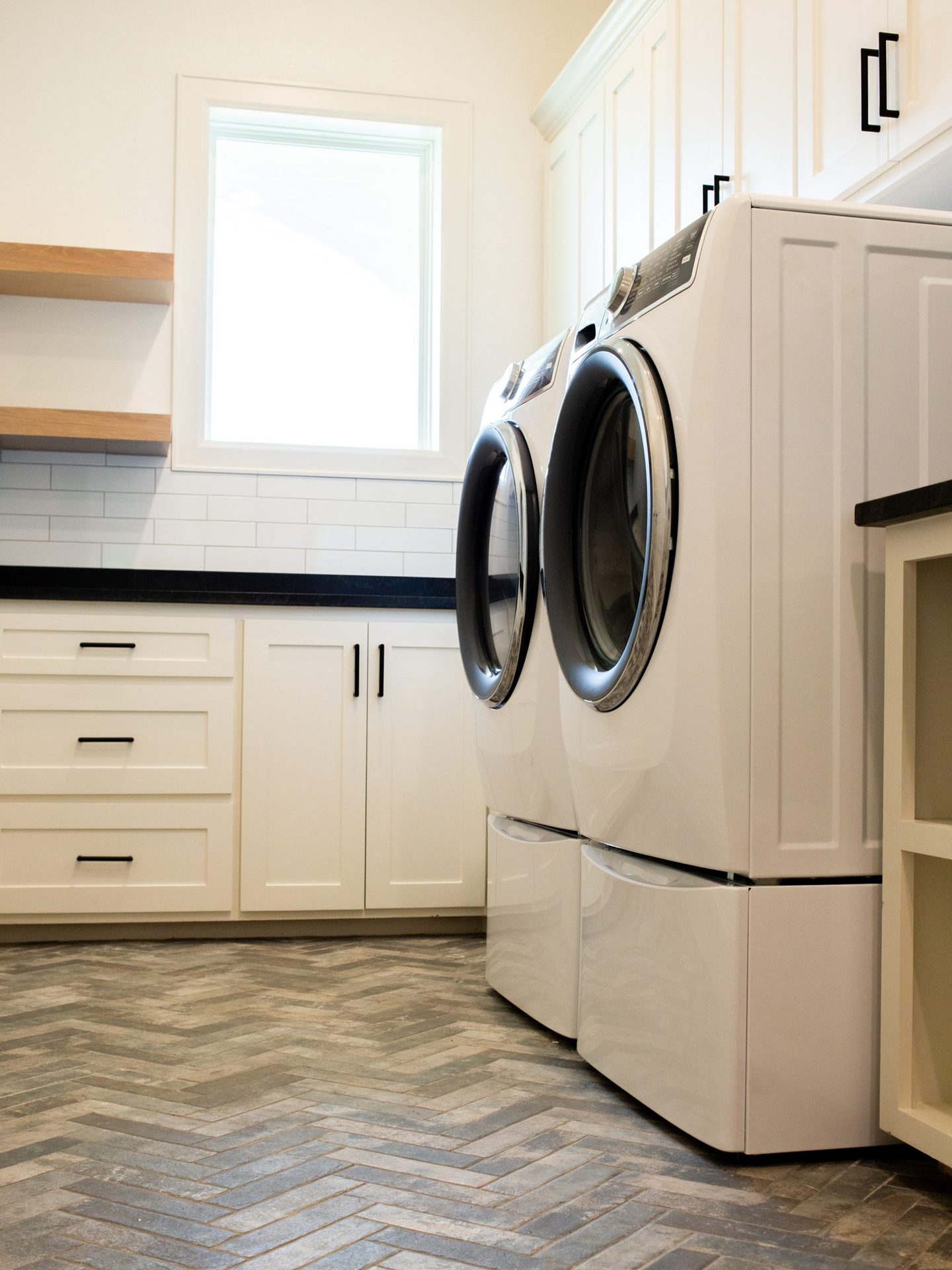 Laundry room with a herringbone brick floor, white cabinetry, open shelving, and front-load washer and dryer.