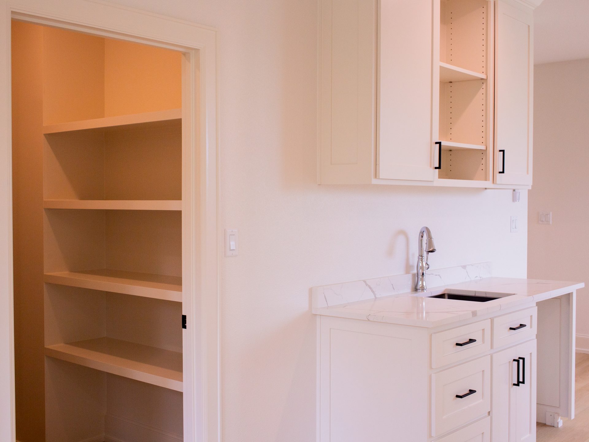 Walk-in pantry with built-in white shelving, adjacent to a butler prep area with quartz counters and a chrome faucet.