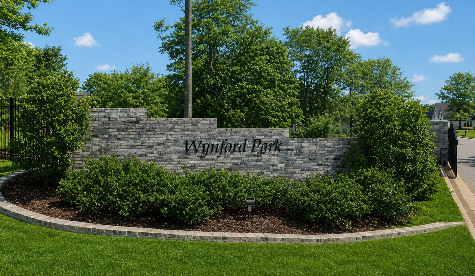 The Wynford Park stone entry gate in summer, with mature landscaping and wrought-iron gates.